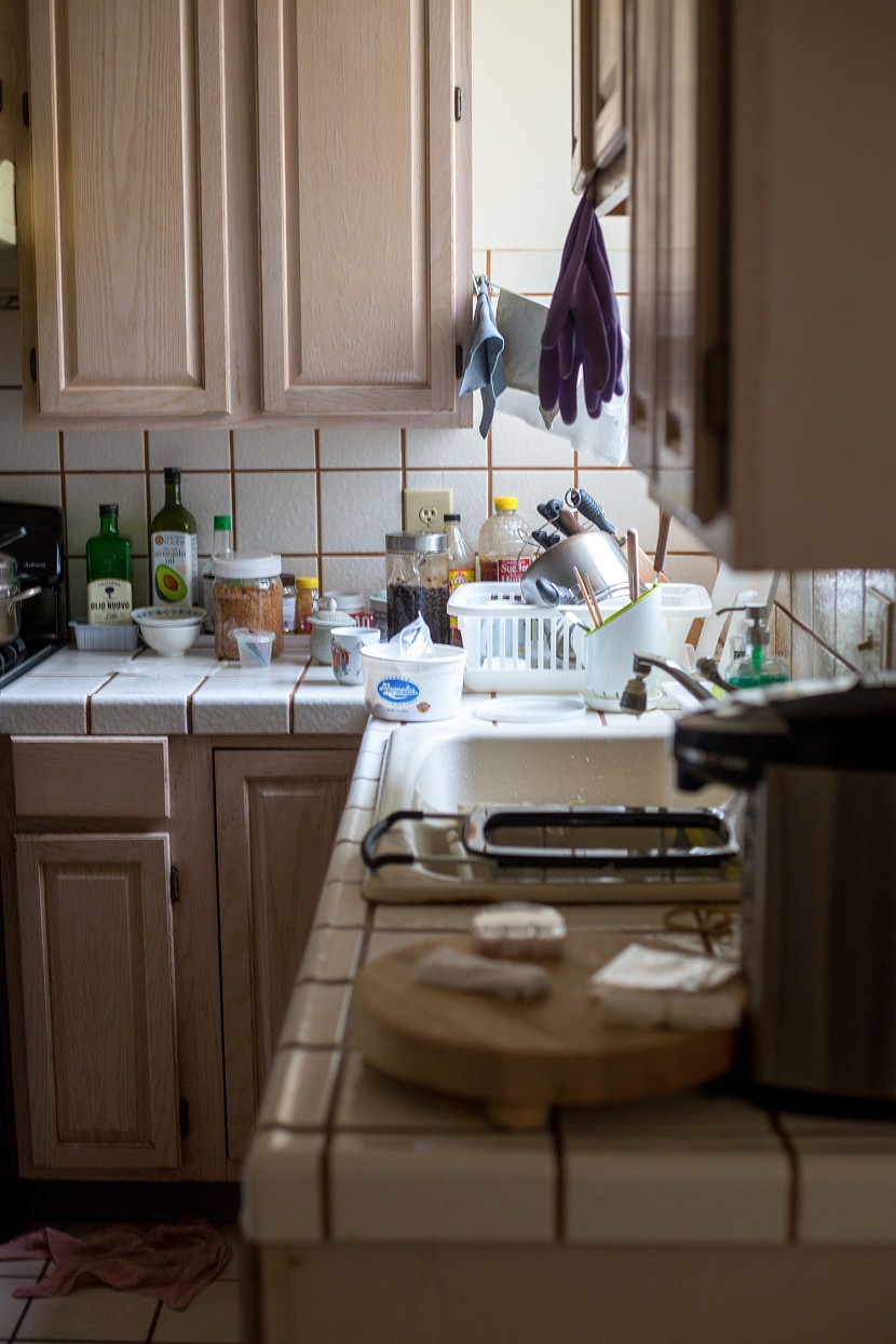 Messy kitchen with poor quality counter and cabinets.